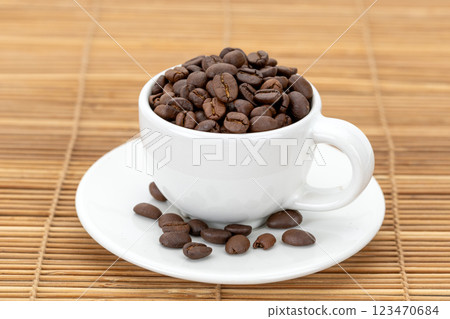 A white ceramic mug filled with roasted coffee beans. 123470684