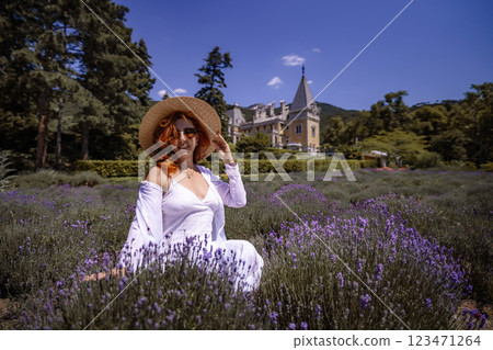 A woman wearing a straw hat sits in a field of purple flowers 123471264