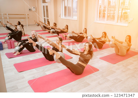 A group of six athletic women doing pilates or yoga on pink mats in front of a window in a beige loft studio interior. Teamwork, good mood and healthy lifestyle concept. 123471347