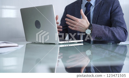 Businessman wearing a blue jacket is focused on online communication via a laptop at a glass desk in a modern office, showcasing productivity and concentration. Business or audit concept Businessman wearing a blue jacket is focused on online communication via a laptop at a glass desk in a modern office, showcasing productivity and concentration. Business or audit concept 123471505
