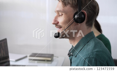 Focused male call center operator in green casual shirt is assisting clients online, providing customer support and answering inquiries. Call center concept Focused male call center operator in green casual shirt is assisting clients online, providing customer support and answering inquiries. Call center concept 123471559