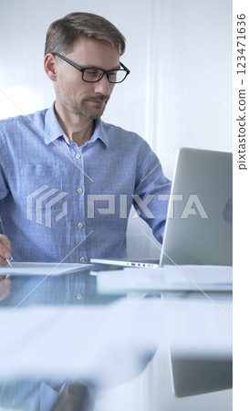 Casual dressed businessman is using a laptop in a contemporary office, with a clean, bright environment that boosts efficiency. Business people concept Casual dressed businessman is using a laptop in a contemporary office, with a clean, bright environment that boosts efficiency. Business people concept 123471636