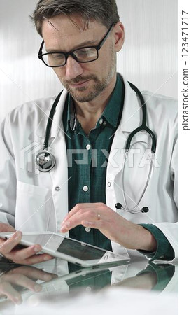Doctor man in green shirt under a white coat using digital tablet in modern healthcare setting, interacting with patient data, vertical portrait. Medicine concept 123471717