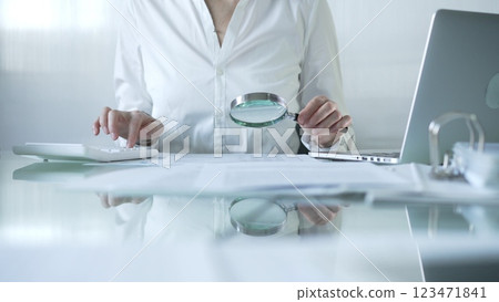 Businesswoman analyzing financial data with magnifying glass and calculator, performing accounting and auditing tasks in office. Audit and taxes theme in business 123471841