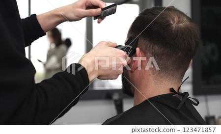 Skilled barber trimming client's hair using electric razor, creating contemporary hairstyle in modern barbershop setting with precise, professional technique Skilled barber trimming client's hair using electric razor, creating contemporary hairstyle in modern barbershop setting with precise, professional technique 123471857