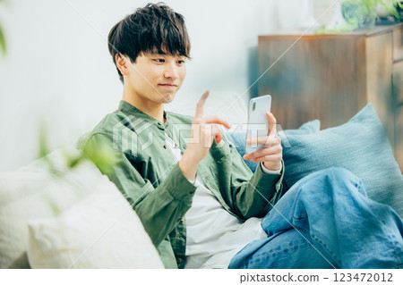 A young man looking at his smartphone in the living room 123472012