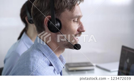 Focused male call center operator in blue casual shirt is assisting clients online, providing customer support and answering inquiries. Call center Focused male call center operator in blue casual shirt is assisting clients online, providing customer support and answering inquiries. Call center 123472039
