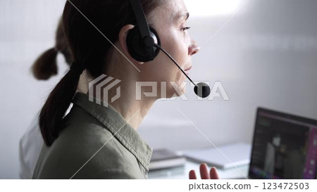 Focused female call center operator in green casual blouse is assisting clients online, providing customer support and answering inquiries. Call center 123472503