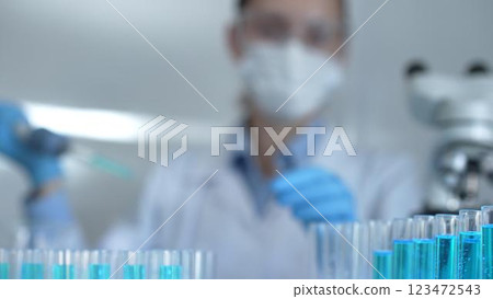 Laboratory tubes are in focus, closeup view. Female scientist researcher is using a micropipette at the background. Medicine and science concept Laboratory tubes are in focus, closeup view. Female scientist researcher is using a micropipette at the background. Medicine and science concept 123472543