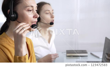 Focused female call center operator in yellow casual blouse is assisting clients online, providing customer support and answering inquiries. Call center concept Focused female call center operator in yellow casual blouse is assisting clients online, providing customer support and answering inquiries. Call center concept 123472583