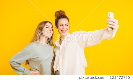 Two young women taking a selfie with smartphone on yellow background 123472730