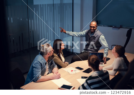 A diverse team of young professionals collaborates in a modern office conference room. Businesspeople discuss strategy, technology, and planning, using laptops to develop an innovative e-commerce 123472916