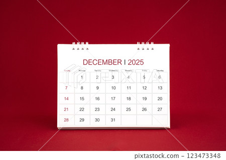 December 2025 white desk calendar stand on dark red background. December 2025 white desk calendar stand on dark red background. 123473348