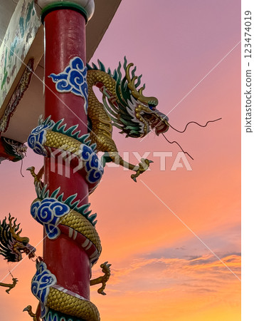 Dragon sculpture, artistically designed with vibrant colors, stands on a pillar against a stunning sunset. 123474019