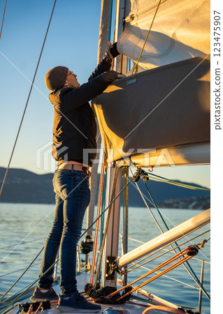 Young man captain operates and controls a sailboat during a journey by sea in winter time in Montenegro 123475907