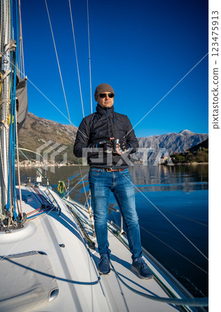 Man holding thermo mug on bow of the yacht during sailing in the morning in winter time in Adriatic sea, relaxation in yachting time Man holding thermo mug on bow of the yacht during sailing in the morning in winter time in Adriatic sea, relaxation in yachting time 123475913