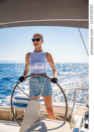 Young woman female captain stands at the helm and controls a sailboat during a journey by sea 123476055