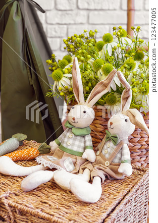 Decorative toy bunnies with carrots on wicker surface on flower bouquet background Decorative toy bunnies with carrots on wicker surface on flower bouquet background 123477005
