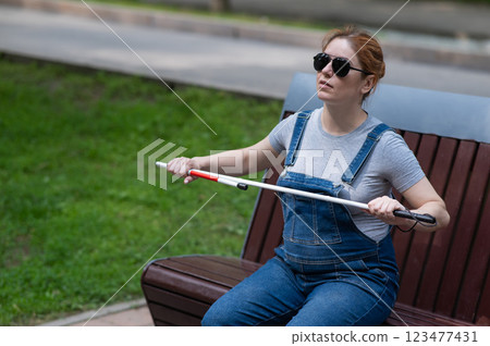 Blind pregnant woman takes out a folding cane while sitting on a bench. Blind pregnant woman takes out a folding cane while sitting on a bench. 123477431