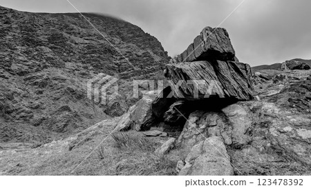 A massive boulder is situated in a rocky landscape, surrounded by uneven ground and steep slopes. A massive boulder is situated in a rocky landscape, surrounded by uneven ground and steep slopes. 123478392