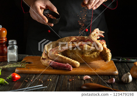 Sprinkling dry spices on a raw duck carcass before cooking in the kitchen. The chef uses his hands to add aromatic seasonings to the bird on the cutting board. A delicious roast duck dinner. 123479198