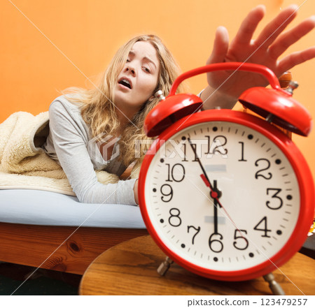 Woman waking up turning off alarm clock in morning Woman waking up turning off alarm clock in morning 123479257