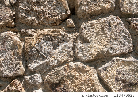 Close-up view of weathered stone wall featuring uneven textures and natural colors in sunlight 123479623
