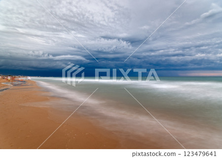 Dramatic clouds hover above the ocean waves gently washing onto the sandy beach shore. Dramatic clouds hover above the ocean waves gently washing onto the sandy beach shore. 123479641