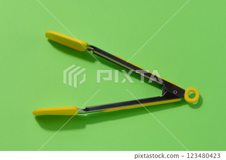 Yellow kitchen tongs with shadow on green background, top view 123480423