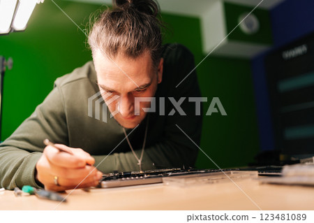 Closeup portrait of skilled technician using tweezers repairing laptop motherboard components in professional electronic workshop setting. Concept of computer hardware, repairing, upgrade, technology 123481089
