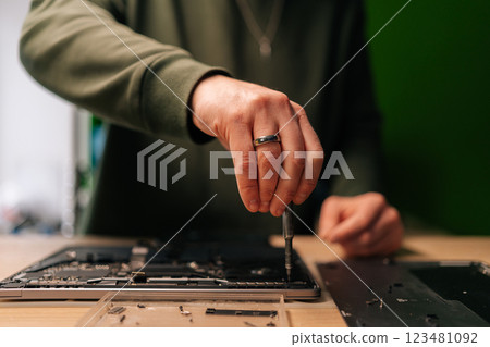 Technician male repairing laptop motherboard, precision screwdriver carefully manipulating electronic components within professional workshop setting. Concept of computer hardware, repairing 123481092