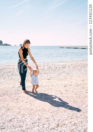 Little boy walks barefoot on a pebble beach holding his mother hands. High quality photo 123481226