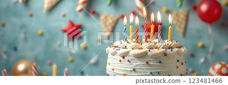 Colorful birthday cake with lit candles surrounded by festive decorations in a cheerful setting 123481466
