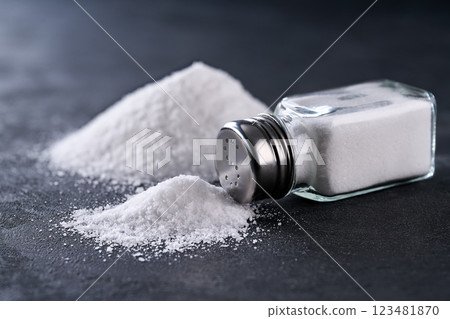 glass salt shaker and crystals of salt on a black table. glass salt shaker and crystals of salt on a black table. 123481870