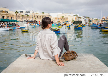 Young woman sitting on the pier and enjoying views of Marsaxlokk, Malta 123481950