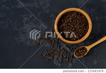 Wooden bowl with cloves spice on a black kitchen table, top view. 123481974