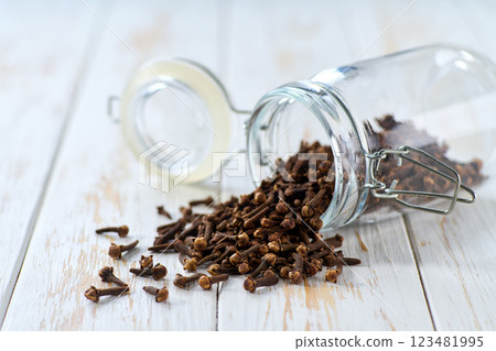 cloves spice spill out of a glass storage jar on a light kitchen table, selective focus. 123481995