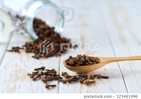 cloves spice in a wooden scoop and in glass storage jar on a light kitchen table, selective focus. cloves spice in a wooden scoop and in glass storage jar on a light kitchen table, selective focus. 123481996