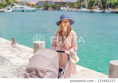 A young mother walks along the scenic waterfront, pushing a baby stroller with her child inside. A peaceful and heartwarming moment of motherhood, relaxation, and outdoor bonding by the sea A young mother walks along the scenic waterfront, pushing a baby stroller with her child inside. A peaceful and heartwarming moment of motherhood, relaxation, and outdoor bonding by the sea 123482217