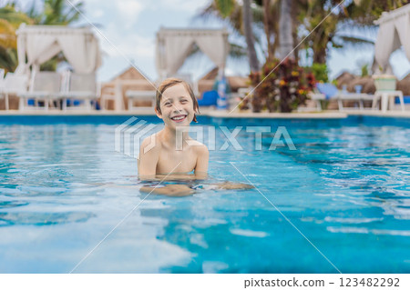 A young boy joyfully swims in a tropical pool surrounded by lush greenery. The vibrant scene captures the essence of summer fun, adventure, and carefree childhood moments in a refreshing outdoor 123482292