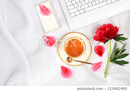 Concept of working from home online. Cozy home desk with laptop, smartphone, tea and a bouquet of delicate peonies and roses. Gift for loved ones and congratulations on the holiday, sunny good 123482460