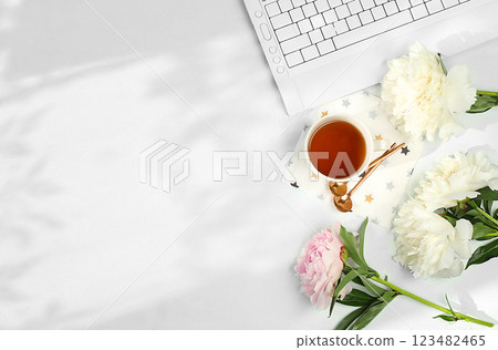 Modern feminine desk, home office. Computer, peony flowers and cup of tea, macaroons on sunny table with long shadows, lifestyle concept, comfortable work from home, template for design, flat lay, 123482465