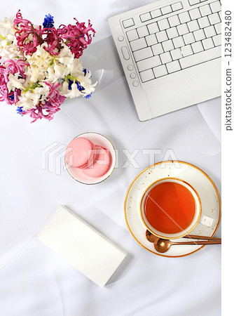 Modern feminine desk, home office. Computer, hyacinth flowers and a cup of tea, macaroons on a sunny table with long shadows, lifestyle concept, comfortable work from home, template for design, flat Modern feminine desk, home office. Computer, hyacinth flowers and a cup of tea, macaroons on a sunny table with long shadows, lifestyle concept, comfortable work from home, template for design, flat 123482480