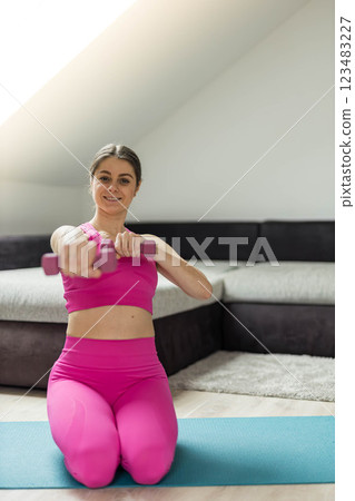 Woman in pink sports outfit doing exercises with dumbbells at home, focusing on strength and fitness 123483227