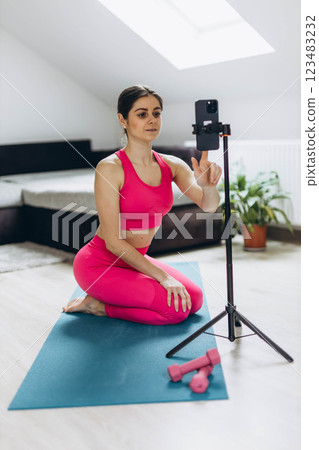 A woman in a pink sports suit conducting an online workout session via her smartphone 123483232