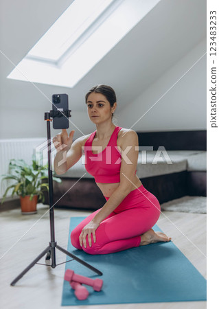 A woman in a pink sports suit conducting an online workout session via her smartphone 123483233