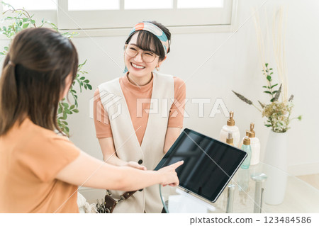 A woman and a hairdresser/stylist looking at an e-book/tablet hair catalog at a beauty salon/hair salon A woman and a hairdresser/stylist looking at an e-book/tablet hair catalog at a beauty salon/hair salon 123484586