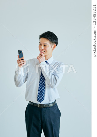 一名二十多歲的年輕人，手托著下巴，手裡拿著智慧型手機 123485211