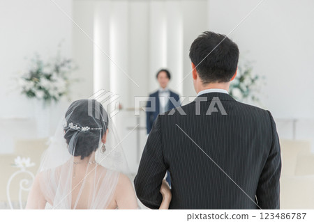 Bride/Bride's woman and father walking along a virgin road to the chapel where the groom waits at the wedding hall Bride/Bride's woman and father walking along a virgin road to the chapel where the groom waits at the wedding hall 123486787