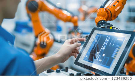 engineer operating a robotic arm using a tablet in a high-tech industrial facility 123489290
